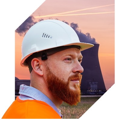 Thoughtful bearded man in a white hard helmet looking over a nuclear plant at sunset