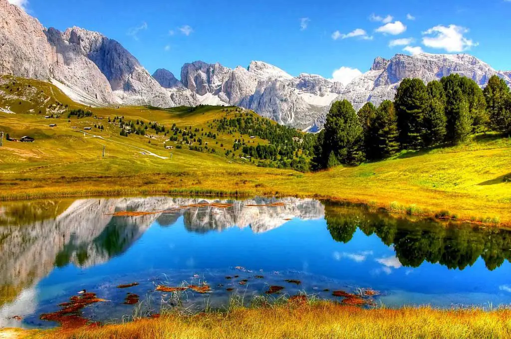 A mountain lake on a sunny day, surrounded by snowy mountains and green hills