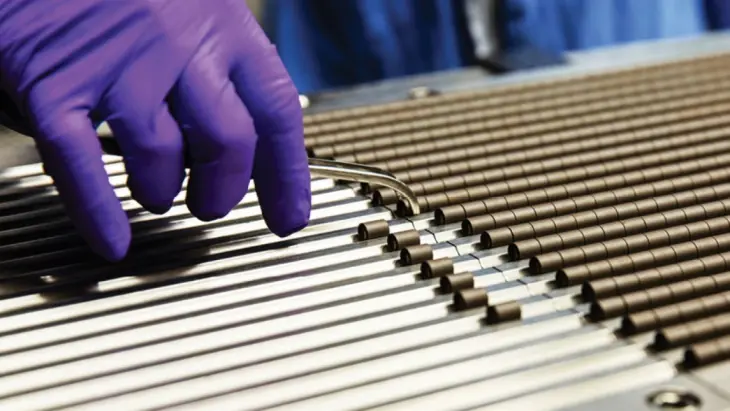 A purple latex gloved hand places small metal rods in metal grooves